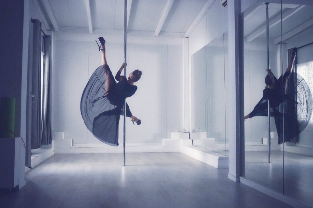 A graceful dancer performs pole dance in a modern studio, showcasing elegance and flexibility.