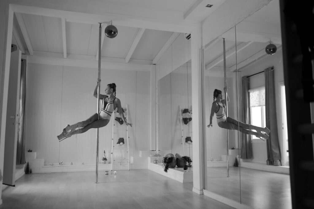 A woman elegantly performs pole dance in a modern, mirrored studio.